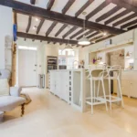 Bright country kitchen with wooden beams across the ceiling and stone flooring throughout.