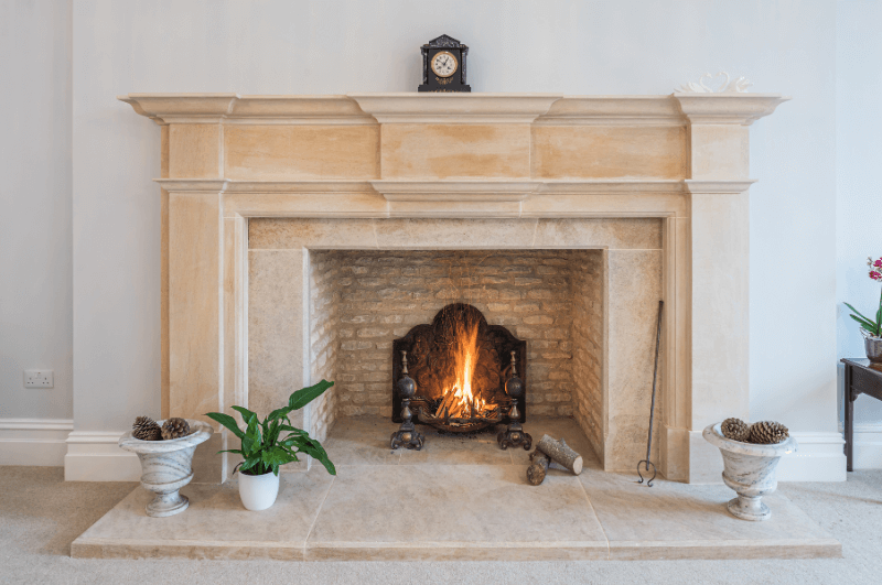 Natural stone fireplace against a white wall with a warm fire glowing inside.