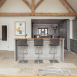 A bright open plan kitchen blending modern furnishings and light grey kitchen cabinetry with a traditional stone floor.