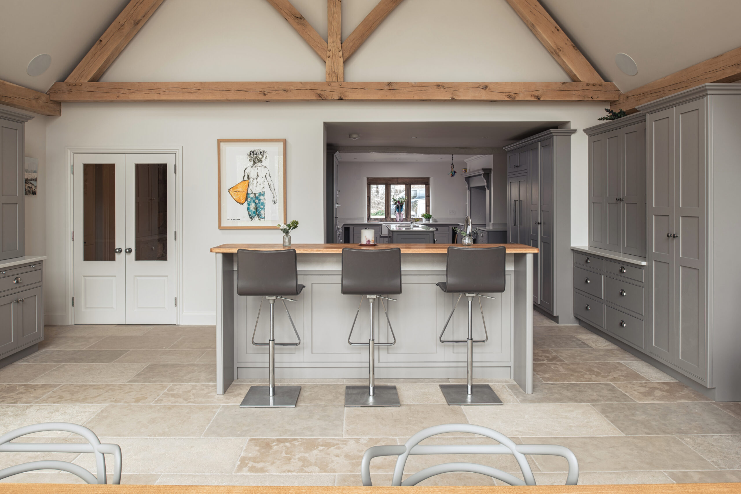 A bright open plan kitchen blending modern furnishings and light grey kitchen cabinetry with a traditional stone floor.